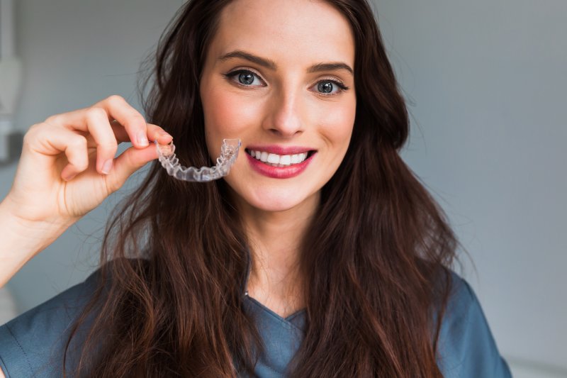 A beautiful, smiling woman holding an Invisalign tray next to her mouth